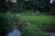 Two people sit on a lush green bank and fish in a small stream in northeastern India.